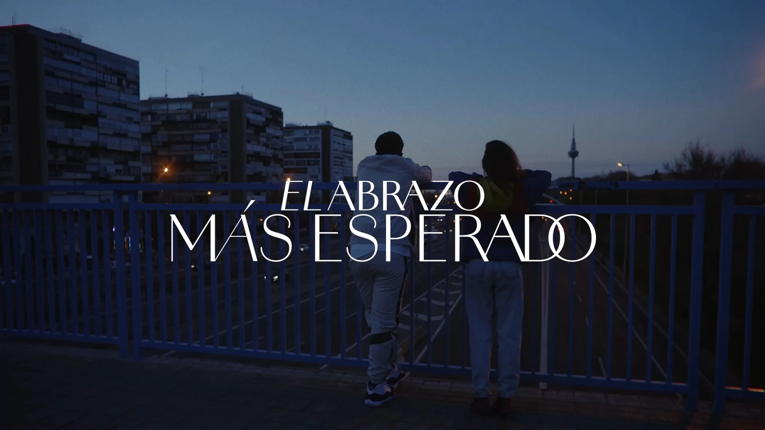 Pieza de campaña con dos personas de espaldas sobre un puente y el título El Abrazo Más Esperado.